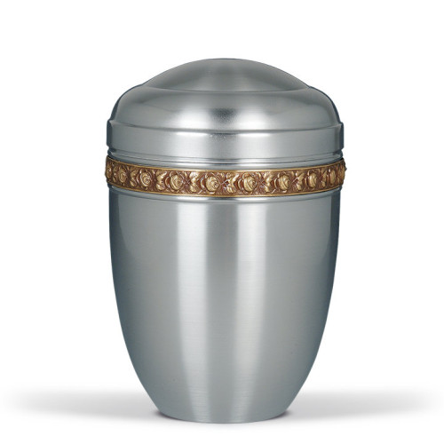 Die Stahlurne ZIHESTA hat eine glänzende silberne Oberfläche und ist mit einem goldenen Messing Rosenband verziert, in einer Gesamtansicht präsentiert.