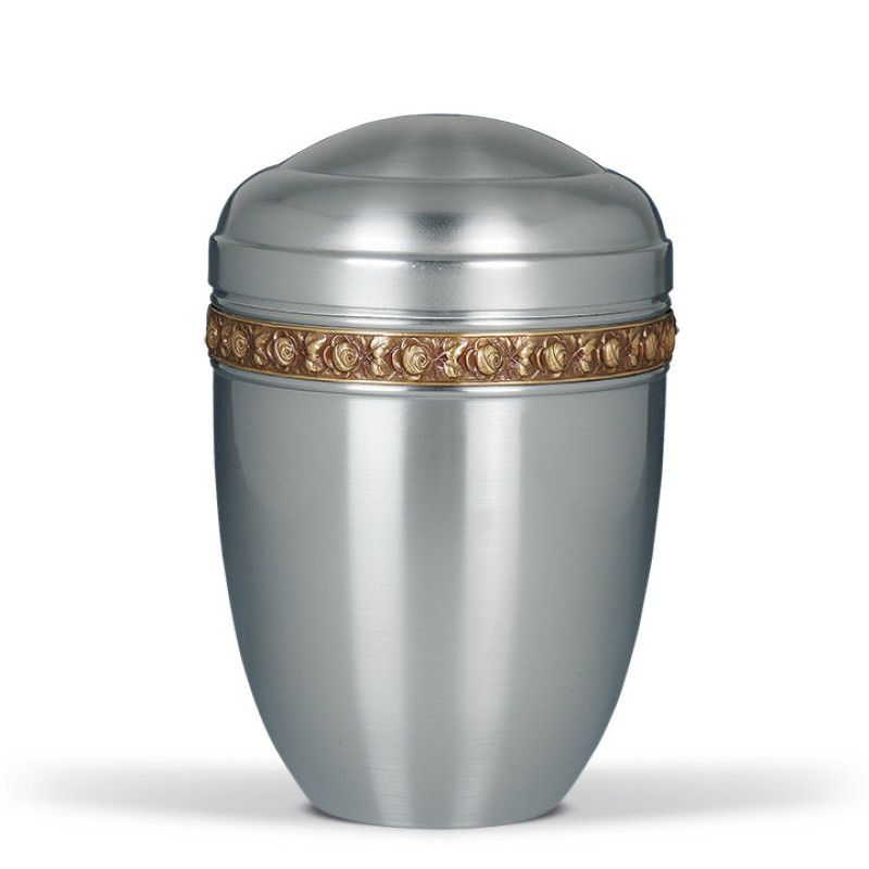 Die Stahlurne ZIHESTA hat eine glänzende silberne Oberfläche und ist mit einem goldenen Messing Rosenband verziert, in einer Gesamtansicht präsentiert.