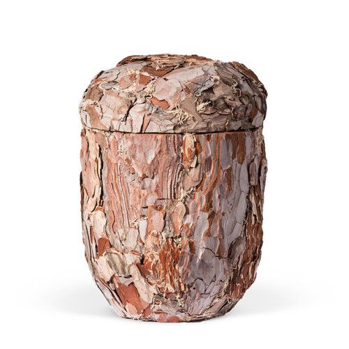 Die Naturstoffurne aus Kiefer ist handgearbeitet, hat eine runde Form und ist mit Rinde bedeckt, die in verschiedenen Brauntönen schimmert.
