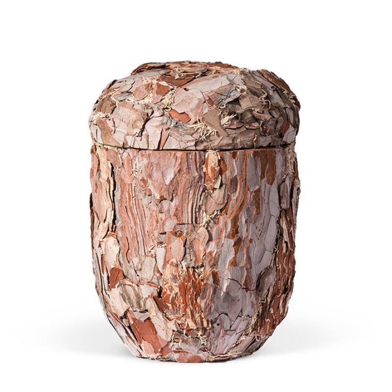 Die Naturstoffurne aus Kiefer ist handgearbeitet, hat eine runde Form und ist mit Rinde bedeckt, die in verschiedenen Brauntönen schimmert.