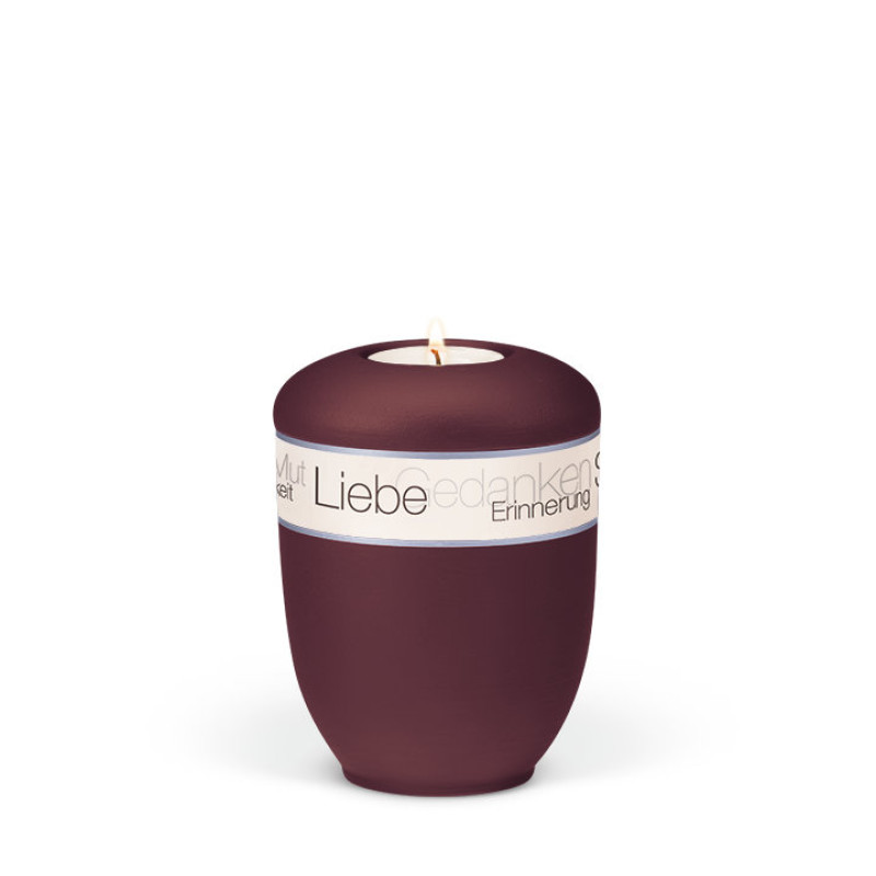 Die weinrote Keramikurne hat eine runde Form, ein samtiges Velours-Finish und ein dekoratives Band mit dem Aufdruck "Trauergedanken" in Rosé, sowie ein Teelicht.