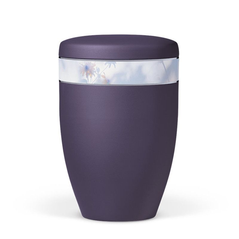 Die violette Naturstoffurne aus Velours hat eine runde Form und ein florales Dekorband, das sich um die Mitte der Urne zieht.