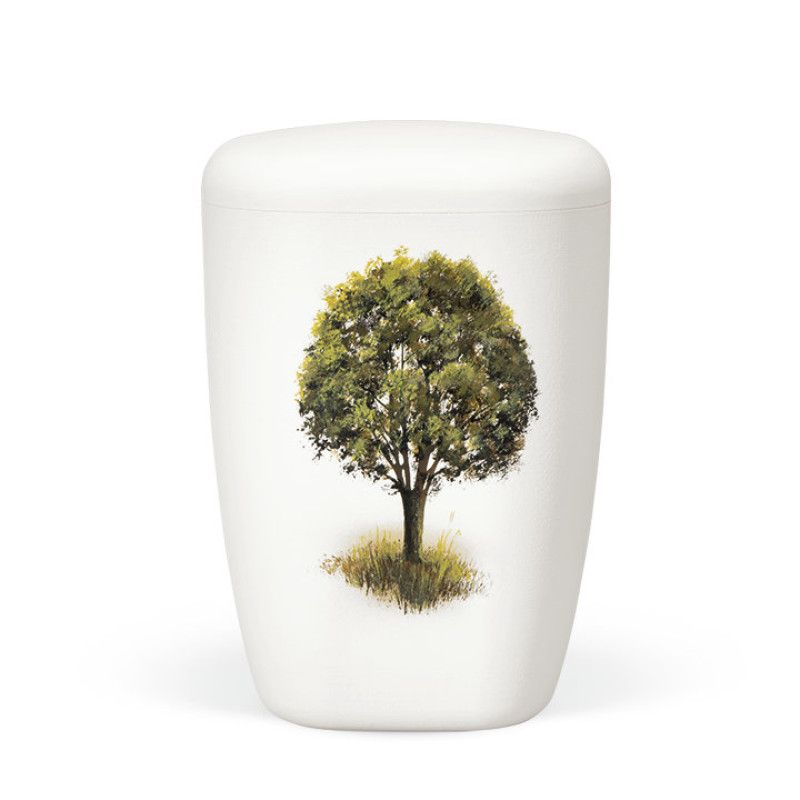 Eine weiße, matte Naturstoffurne mit handbemaltem Baum auf einer Wiese, in ovaler Form und mit einem leicht gewölbten Deckel.