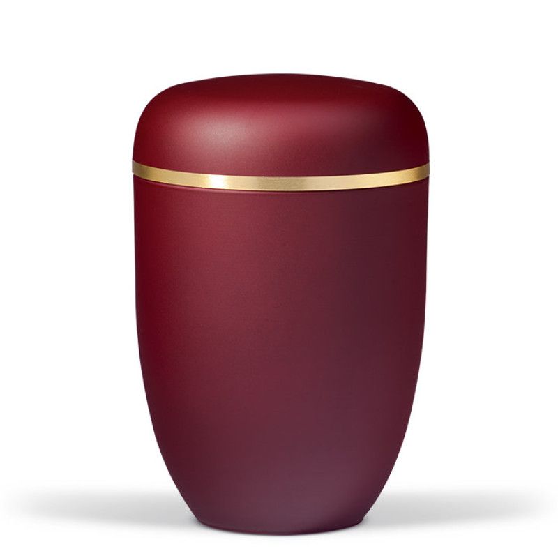 Die Weinrote Stahlurne hat eine ovale Form, eine matte Velours-Oberfläche und ist mit einem gebürsteten Goldband verziert.