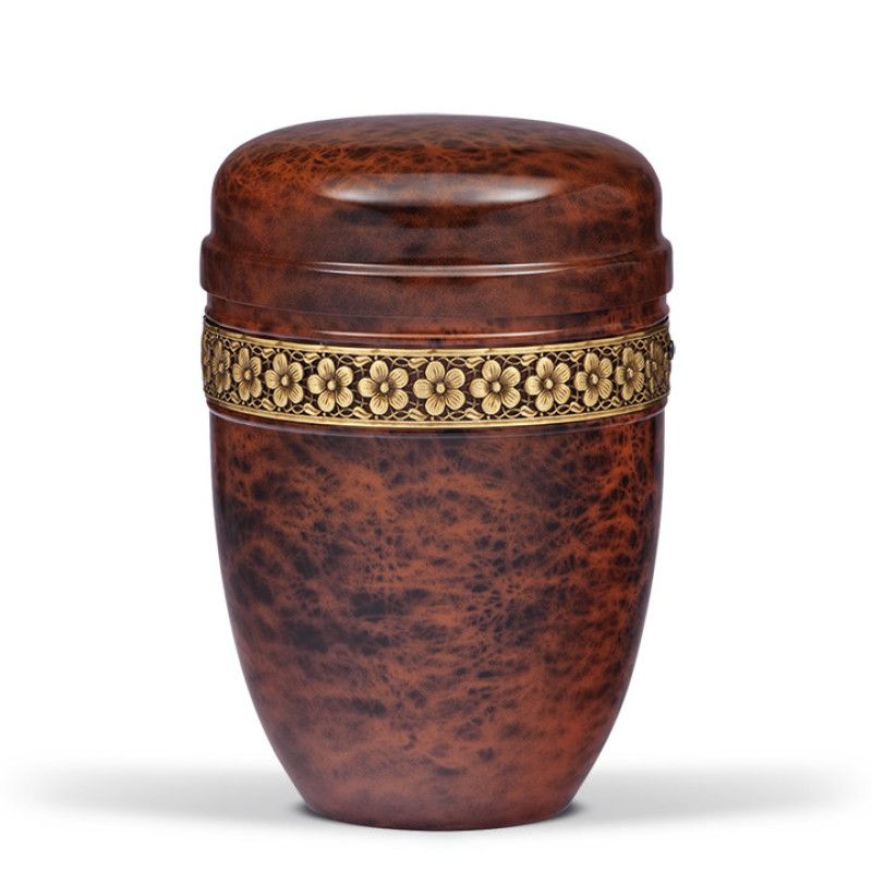 Die Stahlurne im Wurzelholzdesign hat eine runde Form, ist braun mit einer glänzenden Oberfläche und ist mit einem goldfarbenen Blumenband verziert.