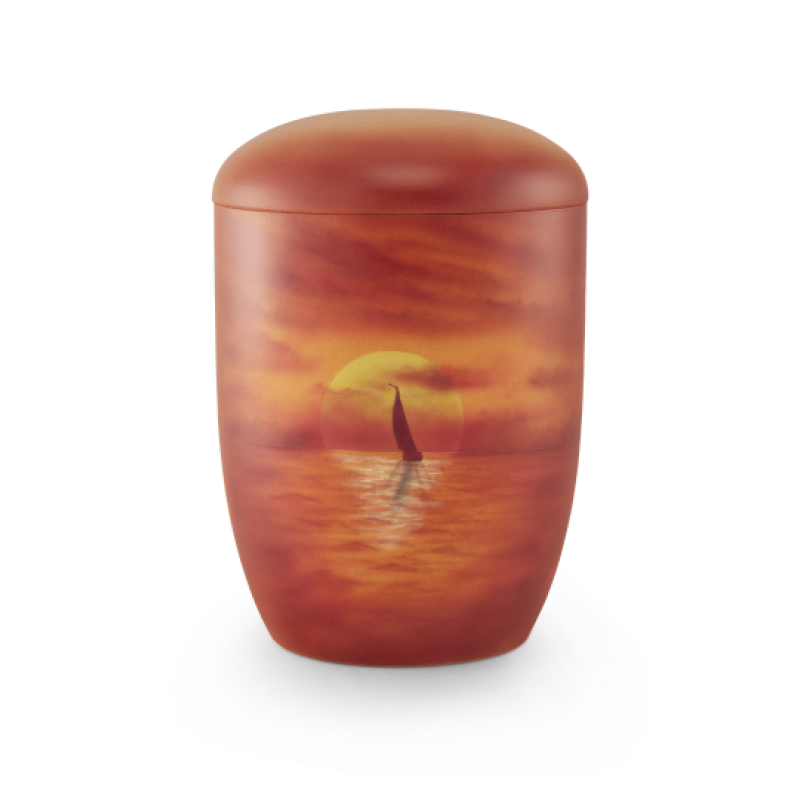 Die Urne aus Anhydrit-Tonolith hat eine ovale Form, ist in warmen Rottönen gehalten und zeigt ein Airbrushmotiv eines Segelbootes vor einem Sonnenuntergang.