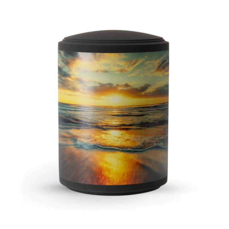 Die Urne aus der Edition Mare hat eine schwarze Samtoberfläche und zeigt ein farbenfrohes Motiv eines Sonnenuntergangs über dem Wasser, mit einem runden, schlichten Design.