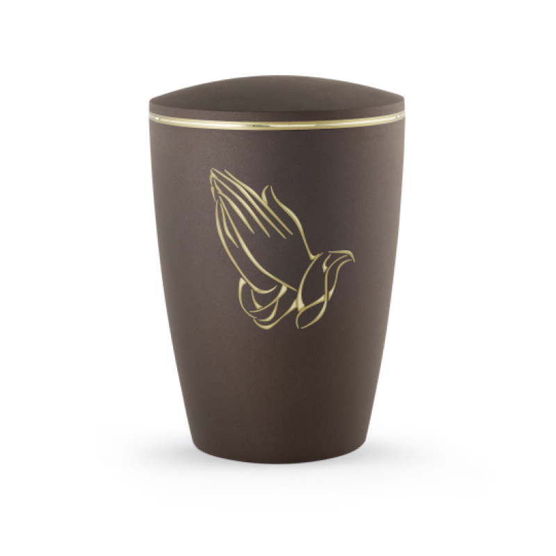 Die Urne aus der Edition Melina in Samtton Cafe hat eine ovale Form, ist aus biologisch abbaubarem Material gefertigt und zeigt betende Hände in goldener Farbe.