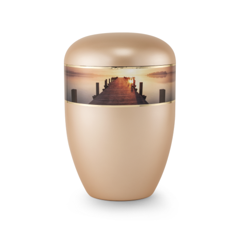 Die Urne in perlmutt apricot hat eine runde Form, einen glänzenden Deckel und zeigt ein Bild eines Stegs im Sonnenuntergang auf einem umlaufenden Band.