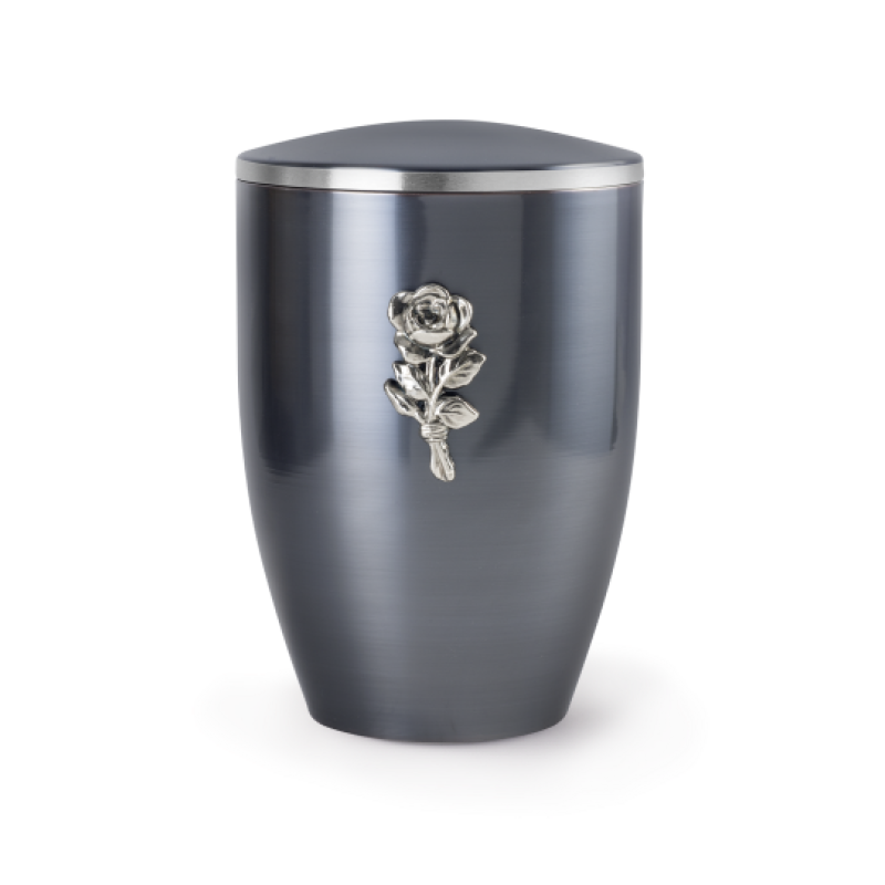 Die Urne der Edition Melina in dark moon lasiert hat eine ovale Form, ist aus Metall gefertigt und zeigt eine silberne Rose als Dekorationsdetail.