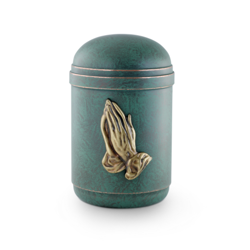 Die Urne ist aus handpatiniertem Kupfer in grünlicher Farbe und zeigt ein goldenes Emblem betender Hände, mit einer runden Form und einem gewölbten Deckel.