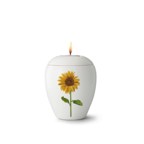 Gedenklicht aus Keramik in weißer Farbe mit einer abgebildeten Sonnenblume, runde Form und brennender Flamme auf der Oberseite.