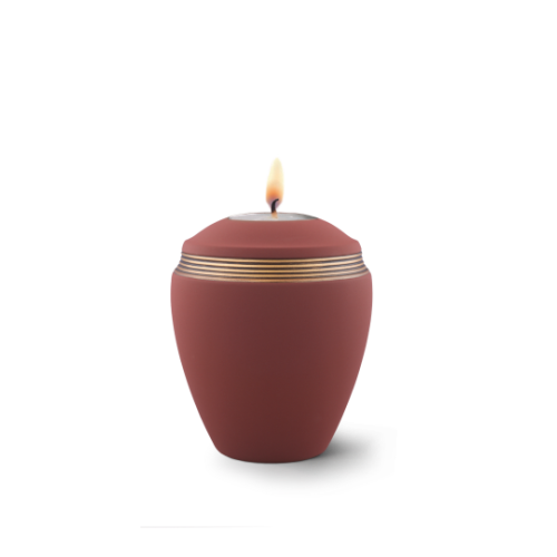 Gedenklicht aus Keramik in Samtton rotbraun mit handbemaltem Dekor in altgold, in Form einer urnenähnlichen Gefäß mit brennender Kerze oben.