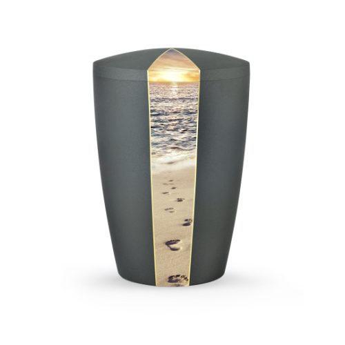 Die Urne aus der Edition Natura in anthrazit hat eine ovale Form und zeigt auf der Vorderseite ein Bild von Fußspuren am Strand mit einem Sonnenuntergang.