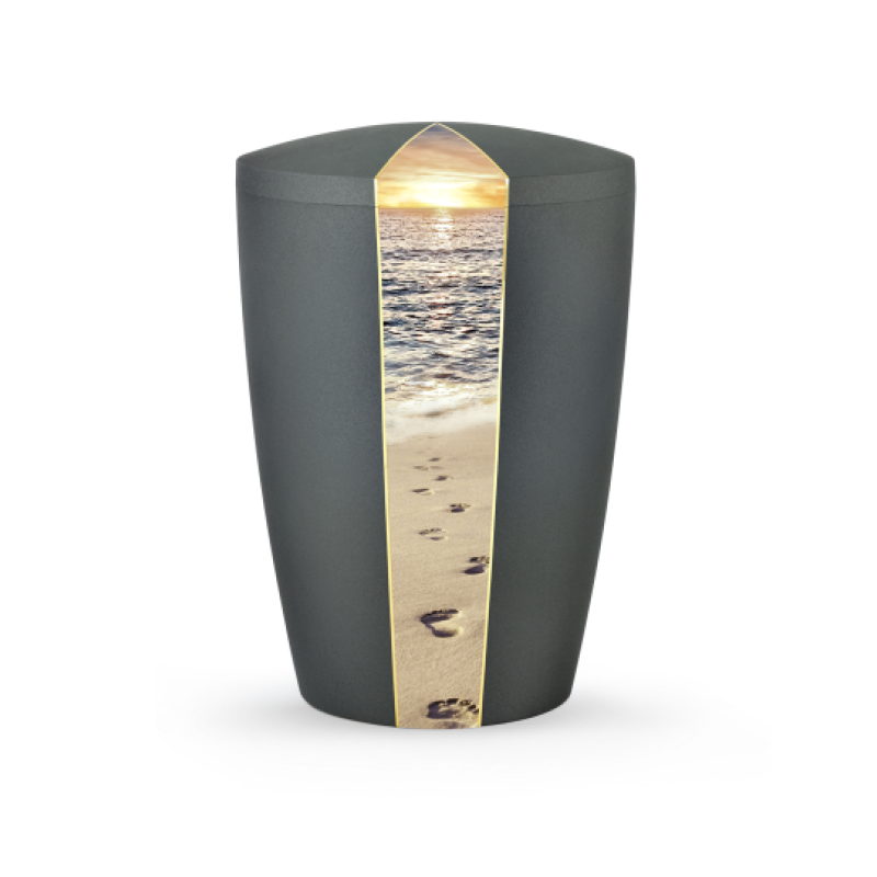Die Urne aus der Edition Natura in anthrazit hat eine ovale Form und zeigt auf der Vorderseite ein Bild von Fußspuren am Strand mit einem Sonnenuntergang.