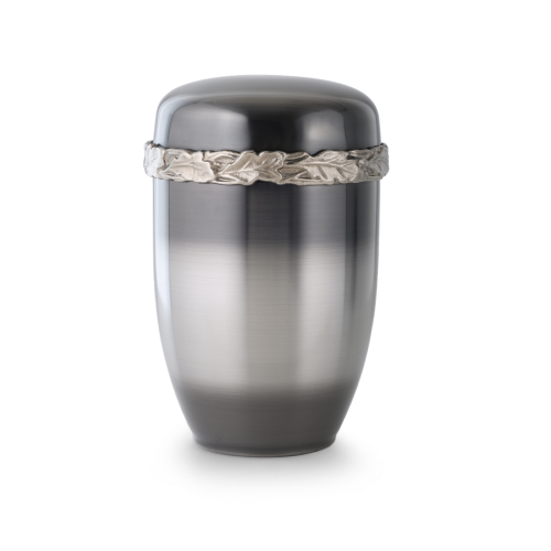 Die Urne Cestal ist galvanisch gefärbt, hat eine ovale Form, eine metallisch glänzende Oberfläche in Grau und ist mit einem Eichenlaub-Gussdekor am Rand verziert.