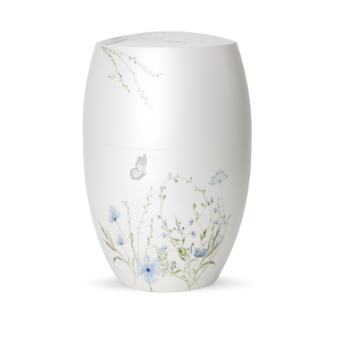 Die Urne in Perlmutt-Mattweiß hat eine ovale Form und ist mit einer blauen Blumenwiese sowie einem Schmetterling verziert, sichtbar in Gesamtansicht.