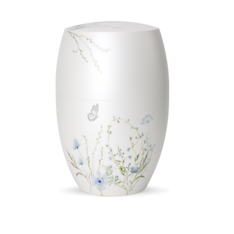 Die Urne in Perlmutt-Mattweiß hat eine ovale Form und ist mit einer blauen Blumenwiese sowie einem Schmetterling verziert, sichtbar in Gesamtansicht.