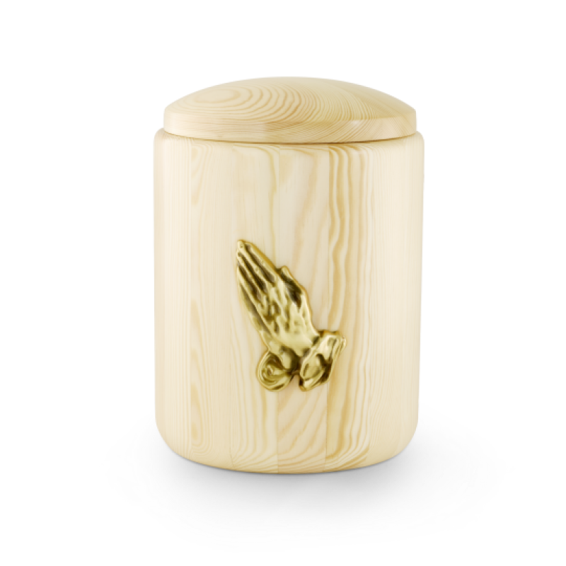 Die Urne aus Kiefernholz hat eine ovale Form, eine helle, natürliche Holzfarbe und zeigt auf der Vorderseite eine goldene, betende Hände-Dekoration.