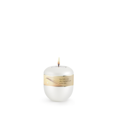 Ein perlmuttfarbenes Gedenklicht in runder Form mit einer goldenen Banderole, auf der der Spruch „Was bleibt, wenn alles…“ zu lesen ist, und einer brennenden Flamme.