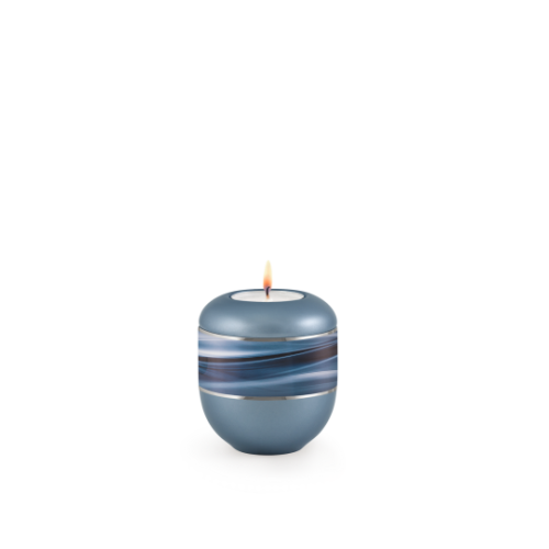 Gedenklicht aus der Edition Wave in perlmutt stahlgrau mit Silberstreifen und Wellenmotiv, rundliche Form, Gesamtansicht mit brennender Kerze.