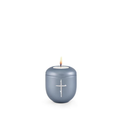 Gedenklicht in perlmutt stahlgrau mit einem Kreuz aus Kristallen, runde Form und leicht gewölbter Oberfläche, mit brennender Kerze oben.