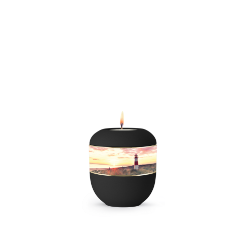 Eine schwarze Porzellanurne in runder Form mit einem abgebildeten Leuchtturm und einer Landschaftsszene, die im oberen Bereich eine Kerzenflamme zeigt.