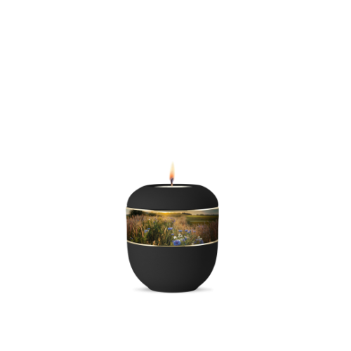 Ein schwarzes Gedenklicht aus Samton mit einer dekorativen Banderole, die Kornblumen und eine Landschaft zeigt, in Gesamtansicht mit brennender Flamme.