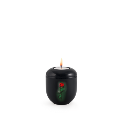 Gedenklicht aus schwarzem Klavierlack mit einer roten Rose auf der Vorderseite, in runder Form und mit brennender Kerze im Inneren.