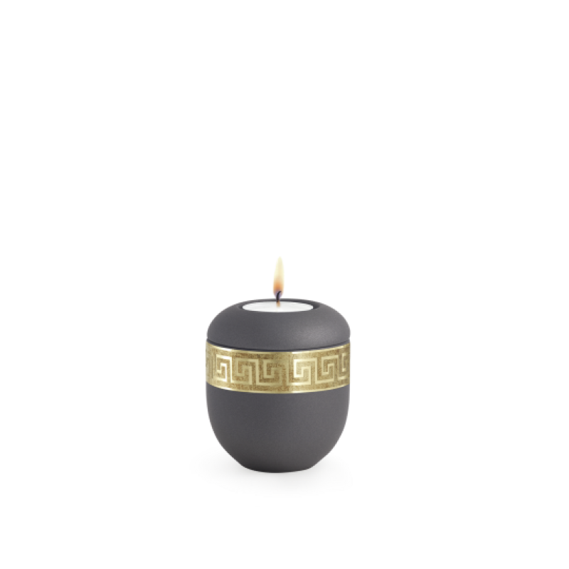 Gedenklicht aus Samton in Anthrazit mit mattgoldenem Mäander-Dekor, rundliche Form, Gesamtansicht mit brennender Kerze.