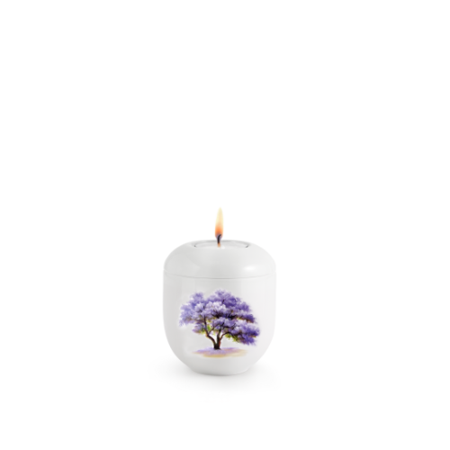 Eine hochglänzende, weiße Gedenkkerze mit einem abgebildeten Blauglockenbaum in lila und einer brennenden Flamme auf der Oberseite.