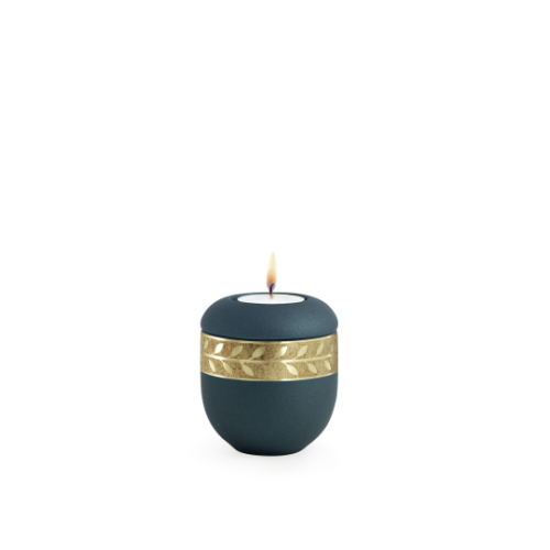 Gedenklicht in velvet Petrol mit mattgoldenem Zweigdekor, altgolden eingefasst, in runder Form und brennender Kerze auf der Oberseite.