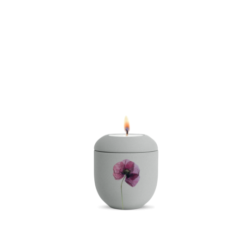Ein graues Gedenklicht aus Keramik mit einer Mohnblumen-Dekoration, das eine flammende Kerze in der oberen Öffnung zeigt, Gesamtansicht.