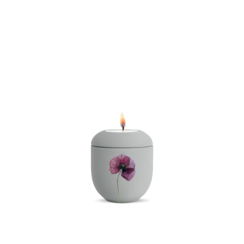 Ein graues Gedenklicht aus Keramik mit einer Mohnblumen-Dekoration, das eine flammende Kerze in der oberen Öffnung zeigt, Gesamtansicht.