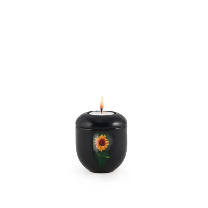 Gedenklicht in Klavierlack schwarz mit einer abgebildeten Sonnenblume, runde Form, brennende Kerze auf der Oberseite, Gesamtansicht.