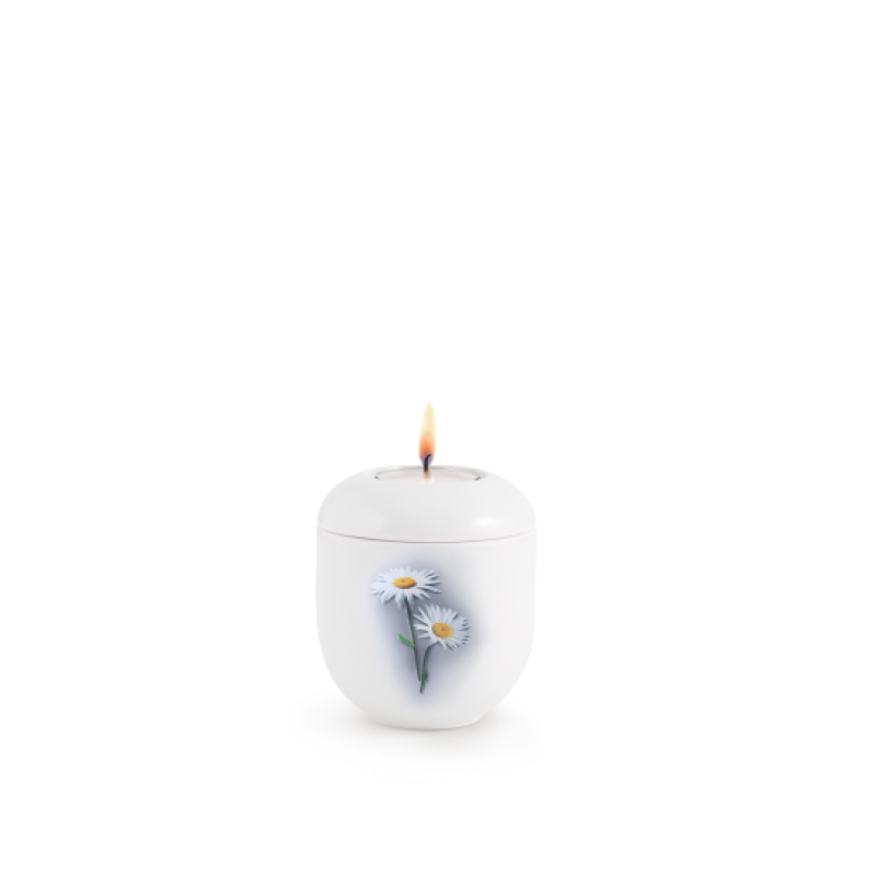 Ein weißes Gedenklicht in runder Form mit einer Margeriten-Dekoration, das an der Oberseite eine Flamme zeigt, Gesamtansicht.
