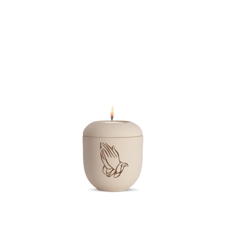Gedenklicht in creme mit betenden Händen als Motiv, aus mattem Material, runde Form, Gesamtansicht mit brennender Flamme.