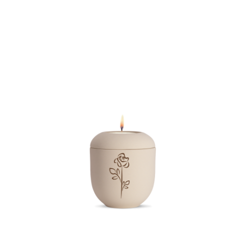Eine cremefarbene Gedenklicht-Urne aus Keramik mit einer eingravierten Rose, Gesamtansicht mit brennender Kerze auf dem Deckel.