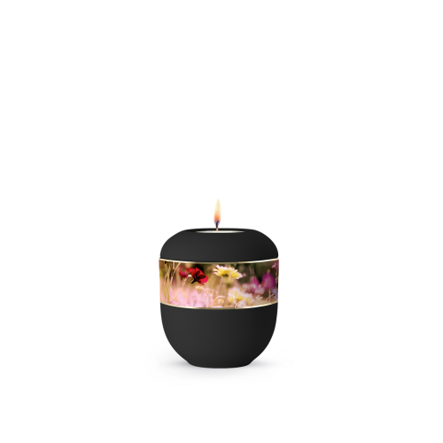 Die schwarze Urne aus Porzellan der Edition Ventura hat eine runde Form, zeigt eine Blumenwiese als umlaufendes Zierband und ist mit einer Kerze versehen.
