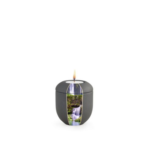 Ein anthrazitfarbenes Gedenklicht mit Wasserfallmotiv, rundlich geformt, aus mattem Material, mit einer flammenbeheizten Öffnung oben.