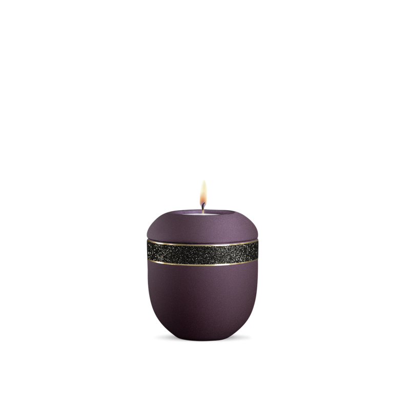 Ein rundes, glitzerndes Gedenklicht in der Farbe Velvet Berry mit schwarzem Dekor und einer brennenden Kerze auf der Oberseite, Gesamtansicht.
