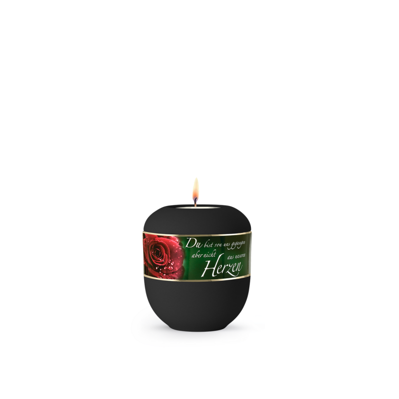 Ein rundes, tiefschwarzes Gedenklicht mit einer brennenden Flamme und einem Aufkleber, der eine rote Rose sowie den Schriftzug „Du bist von uns gegangen… im Herzen“ zeigt.