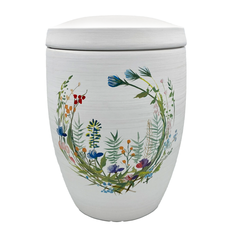 Die Alto Urne ist oval, weiß und mit einem bunten Wildblumenkranz aus verschiedenen Pflanzenmotiven verziert, die die gesamte Vorderseite schmücken.