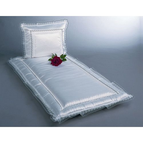 Ein weißes Serge-Bett mit einer gesteppten Matratze und einem Kopfkissen, verziert mit einer schwarzen Borte, auf dem eine rote Rose liegt.