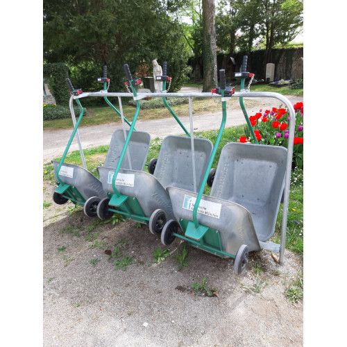 Pfandstation mit 6 Wagen aus grauem Kunststoff, montiert auf einem stabilen Metallgestell in grüner Farbe, Gesamtansicht im Freien mit Blumen im Hintergrund.