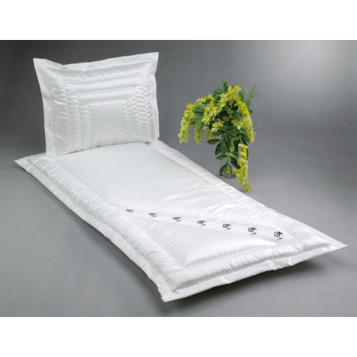 Ein weißes Serge-Bett mit einer gesteppten Oberfläche und einem Kissen, verziert mit kleinen Stiefmütterchen aus Organza, sowie einer Blumenarrangement daneben.