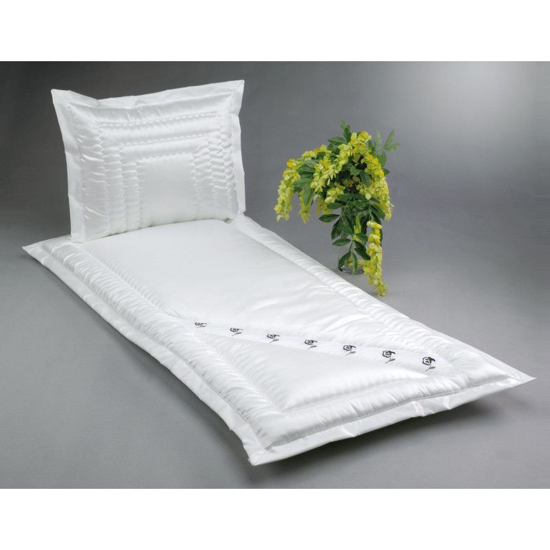 Ein weißes Serge-Bett mit einer gesteppten Oberfläche und einem Kissen, verziert mit kleinen Stiefmütterchen aus Organza, sowie einer Blumenarrangement daneben.