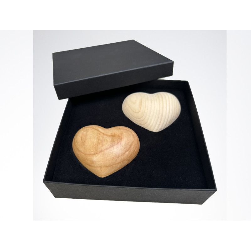 Eine schwarze Überreichungsbox mit Deckel enthält zwei hölzerne Handschmeichler in Herzform, einer in hell und einer in dunkelbraun.