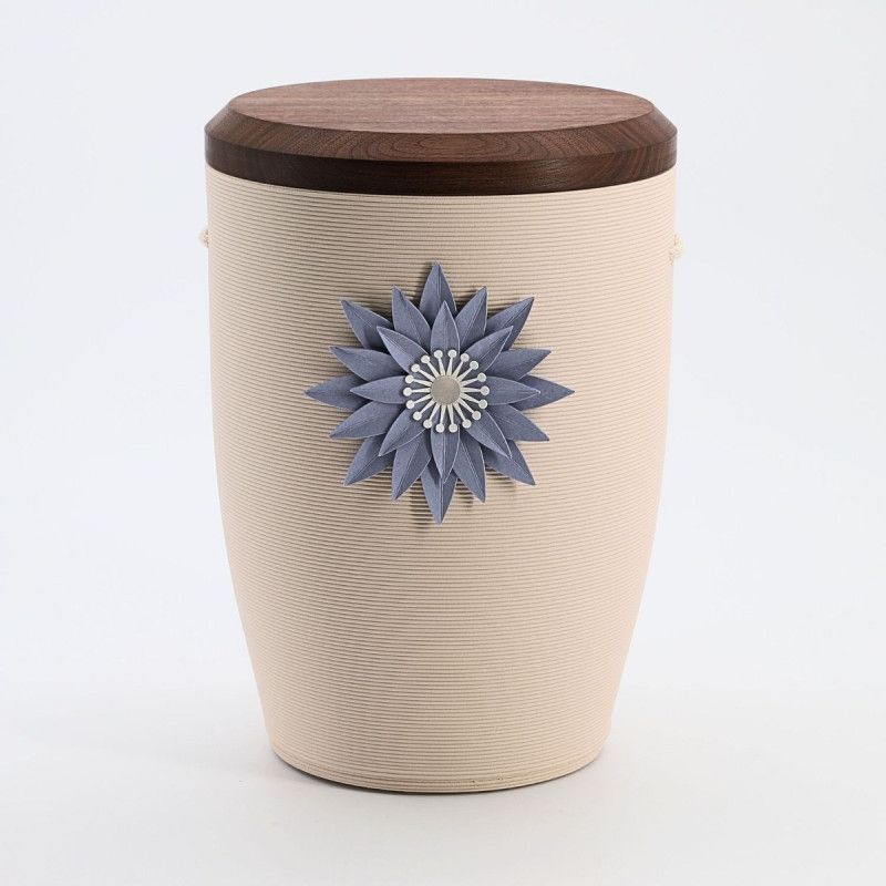 Die Urne Stille Blüte in Blau und Creme hat eine runde Form, eine strukturierte Oberfläche und ist mit einer blauen Blütenapplikation sowie einem Holzdeckel versehen.