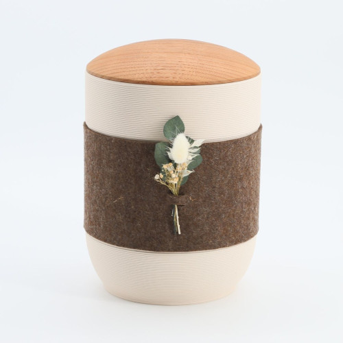 Die Urne Mira Band in Braun und Creme aus Tonerde hat eine runde Form, eine Holzdeckel und ist mit einem braunen Filzband sowie einer floralen Dekoration versehen.